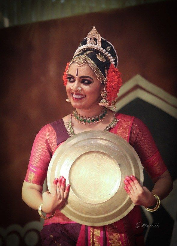 Medha Mayuri in magenta and gold, holding a brass plate.